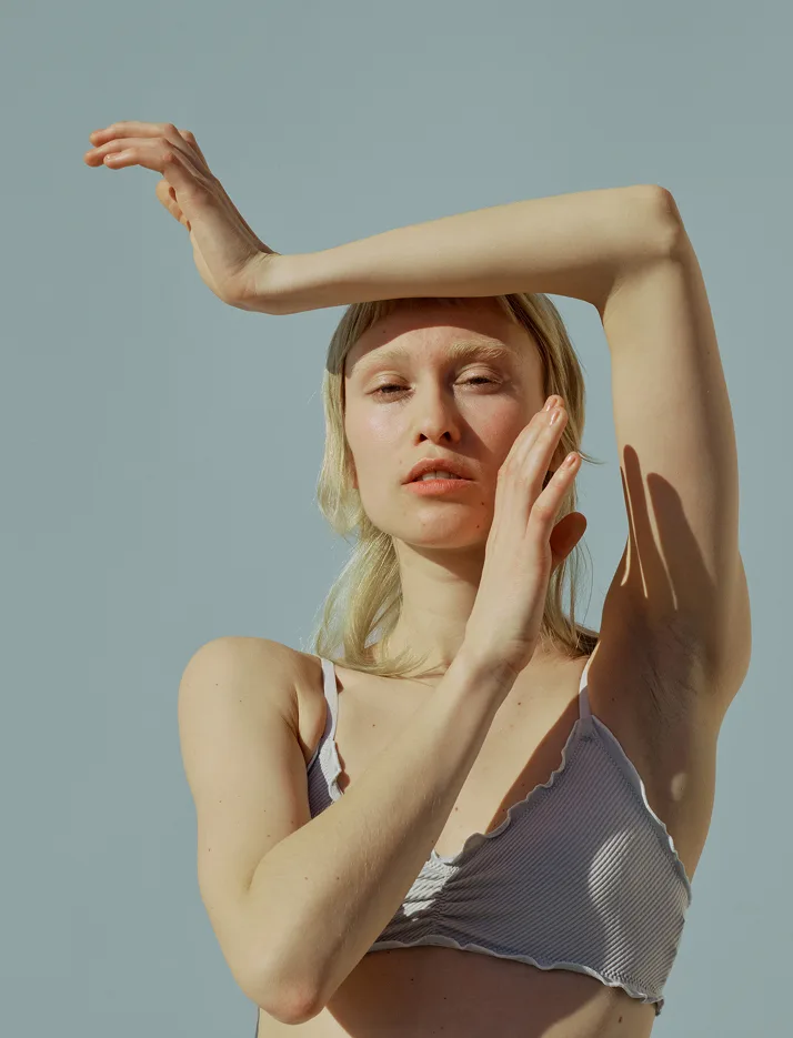 Model framing her face with raised arms in soft sunlight